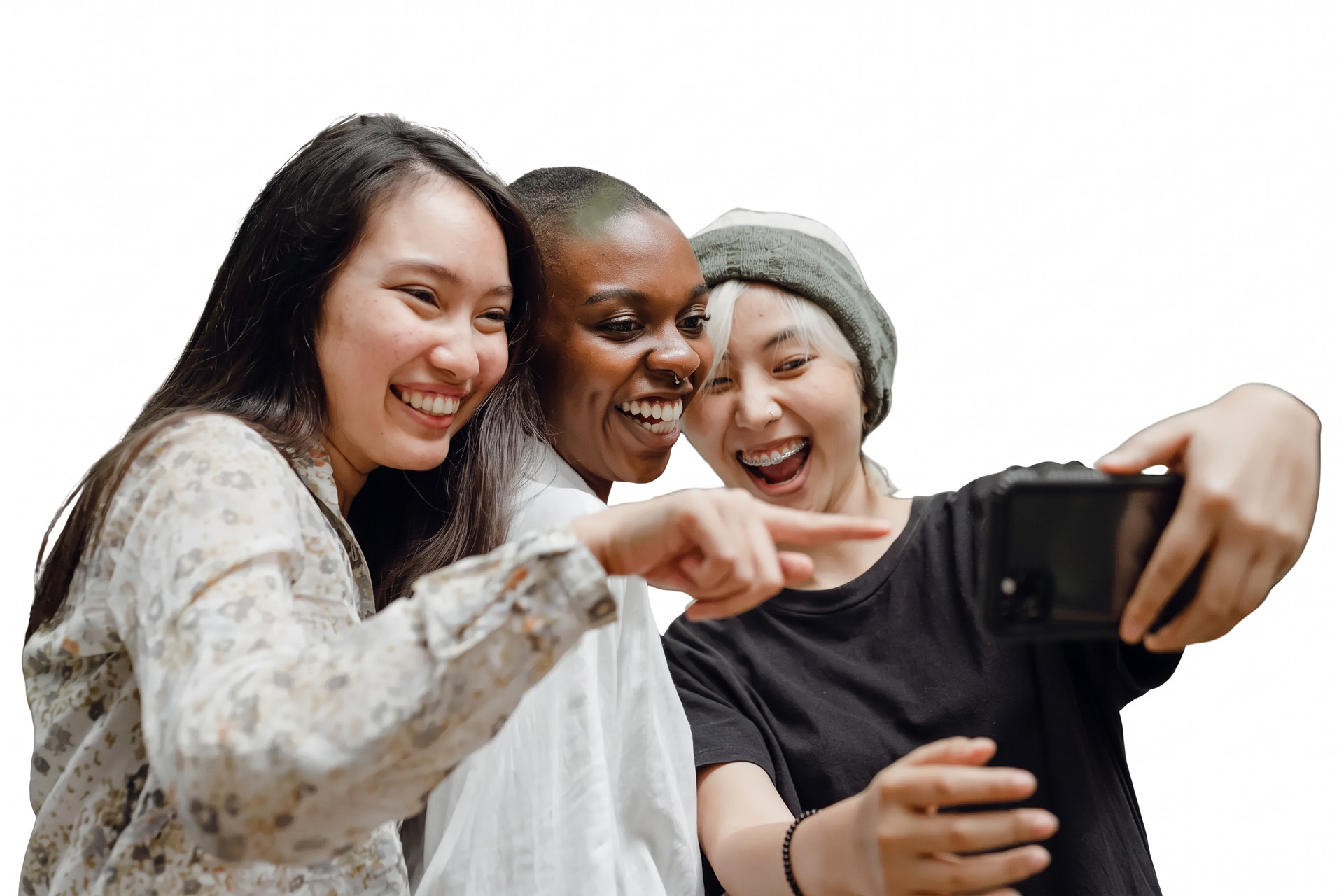 Three women laughing together while looking at a phone